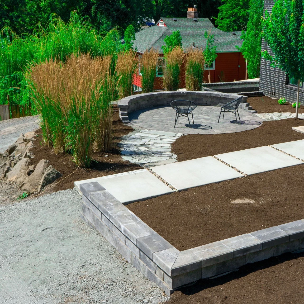 Round patio surrounded by tall grasses on the left and a walkway with bark on the right