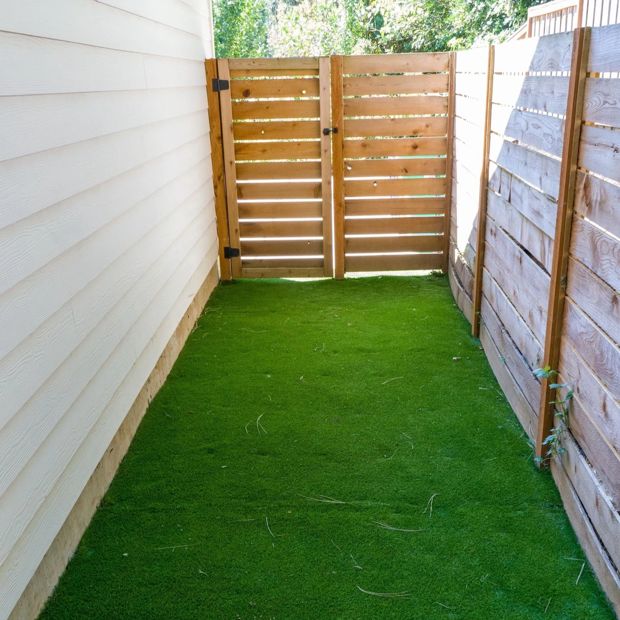 Side of a house with a fence gate and artificial turf in view