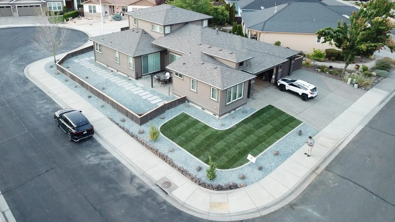 Aerial view of a suburban house with a newly landscaped front yard featuring a striped green lawn, gravel beds, stepping-stone paths, a concrete driveway, and parked cars on a residential street.