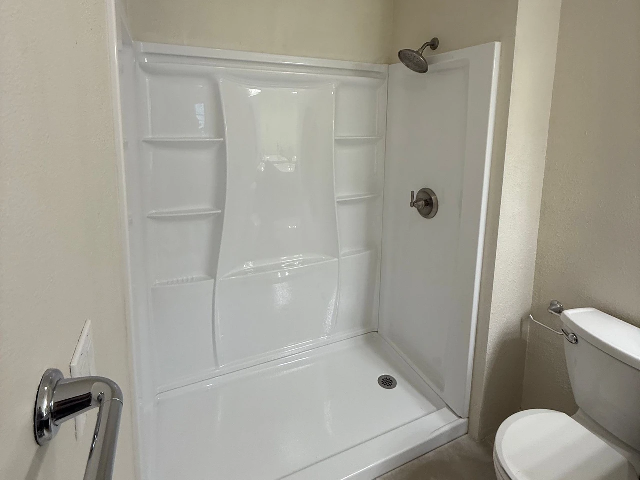 New fiberglass shower with a shower head and toilet in view