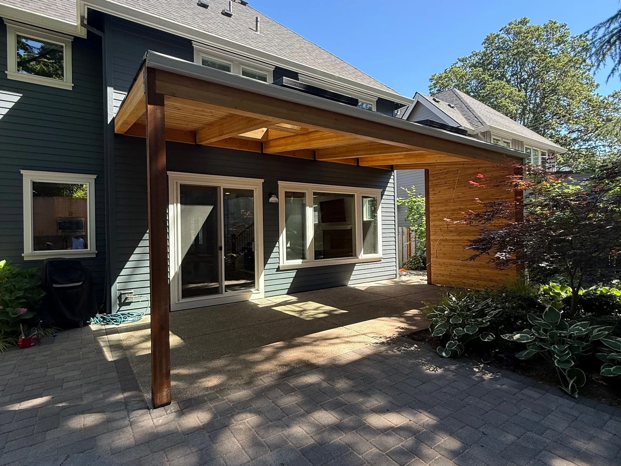 patio cover on a blue house with bushes to the side