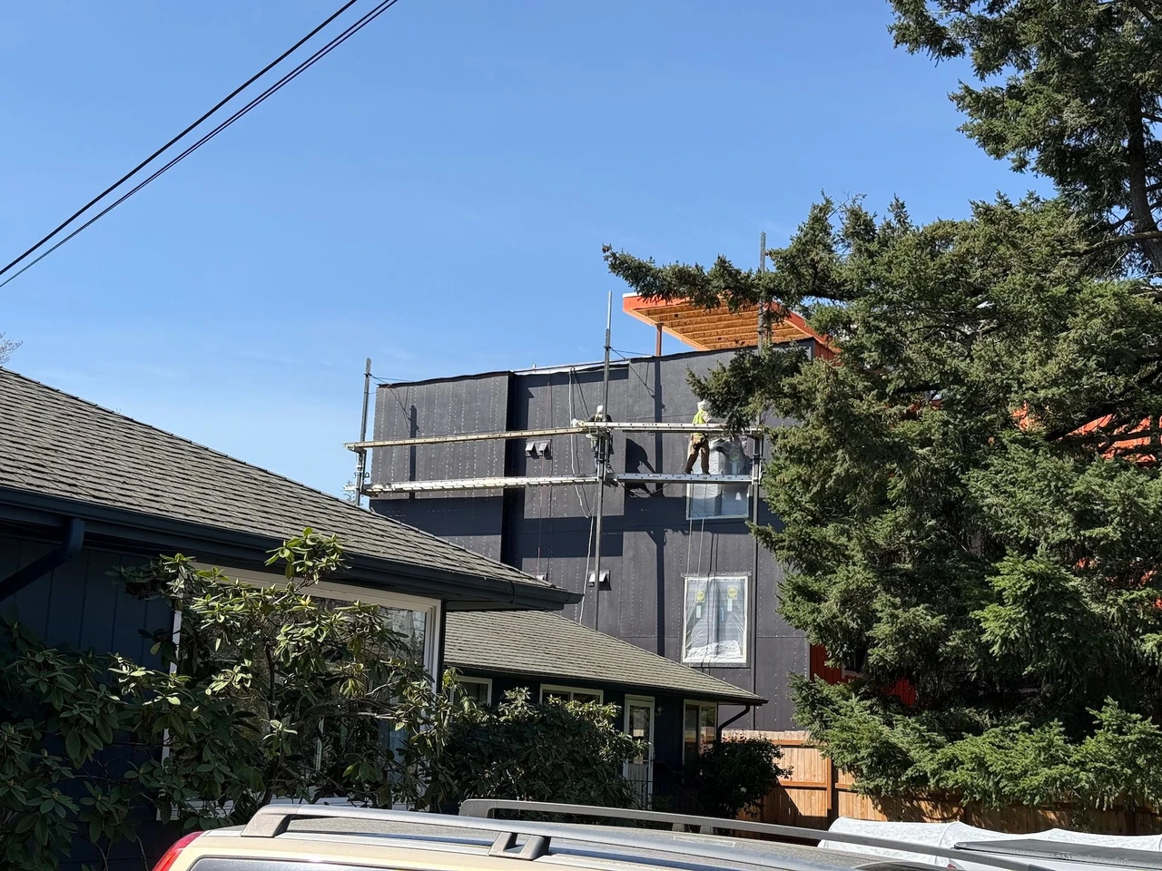 A gray commercial building being painted by 2 workers on scaffolding