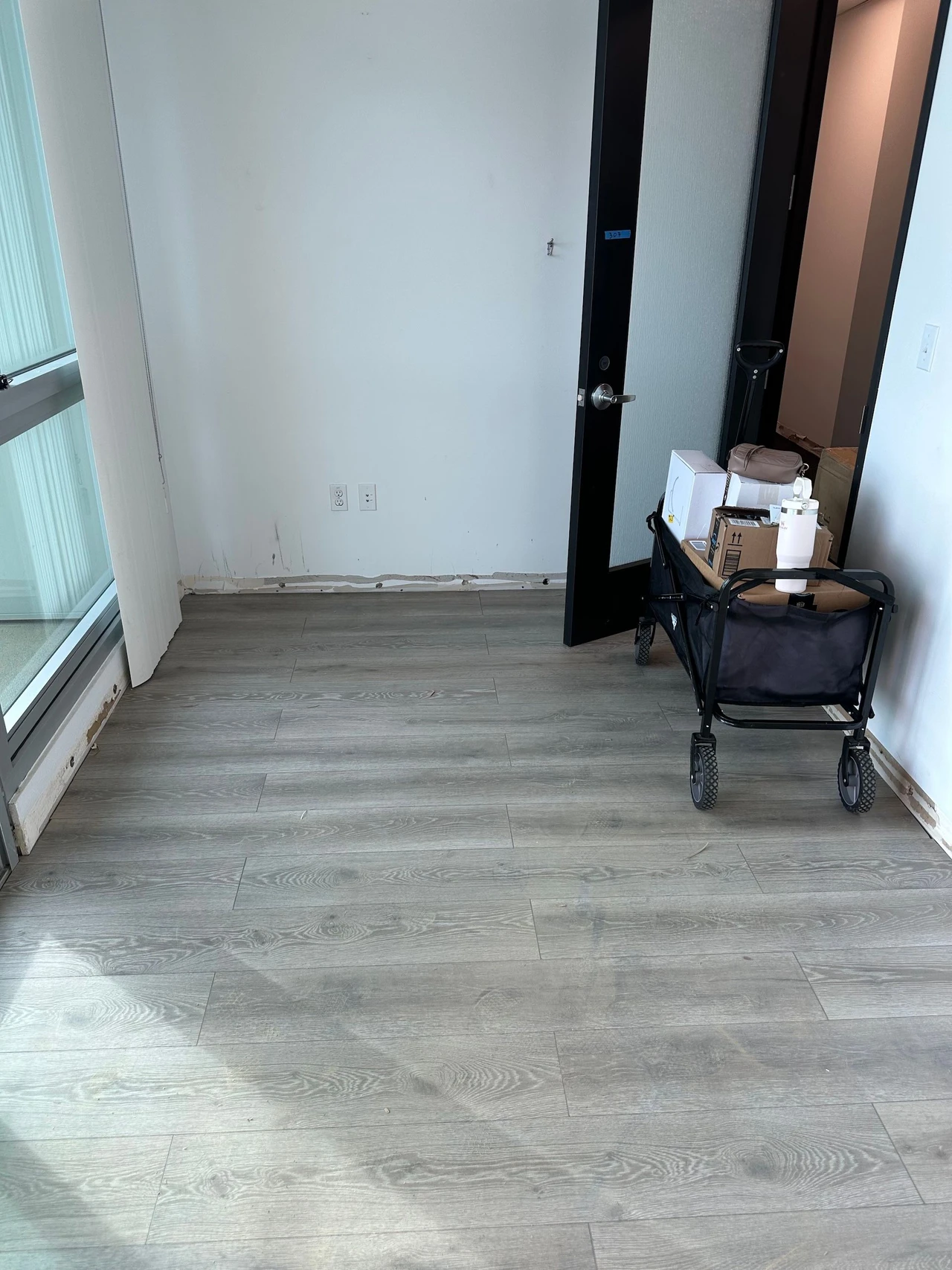 Small office space with gray laminate flooring and a cart by the door in the corner