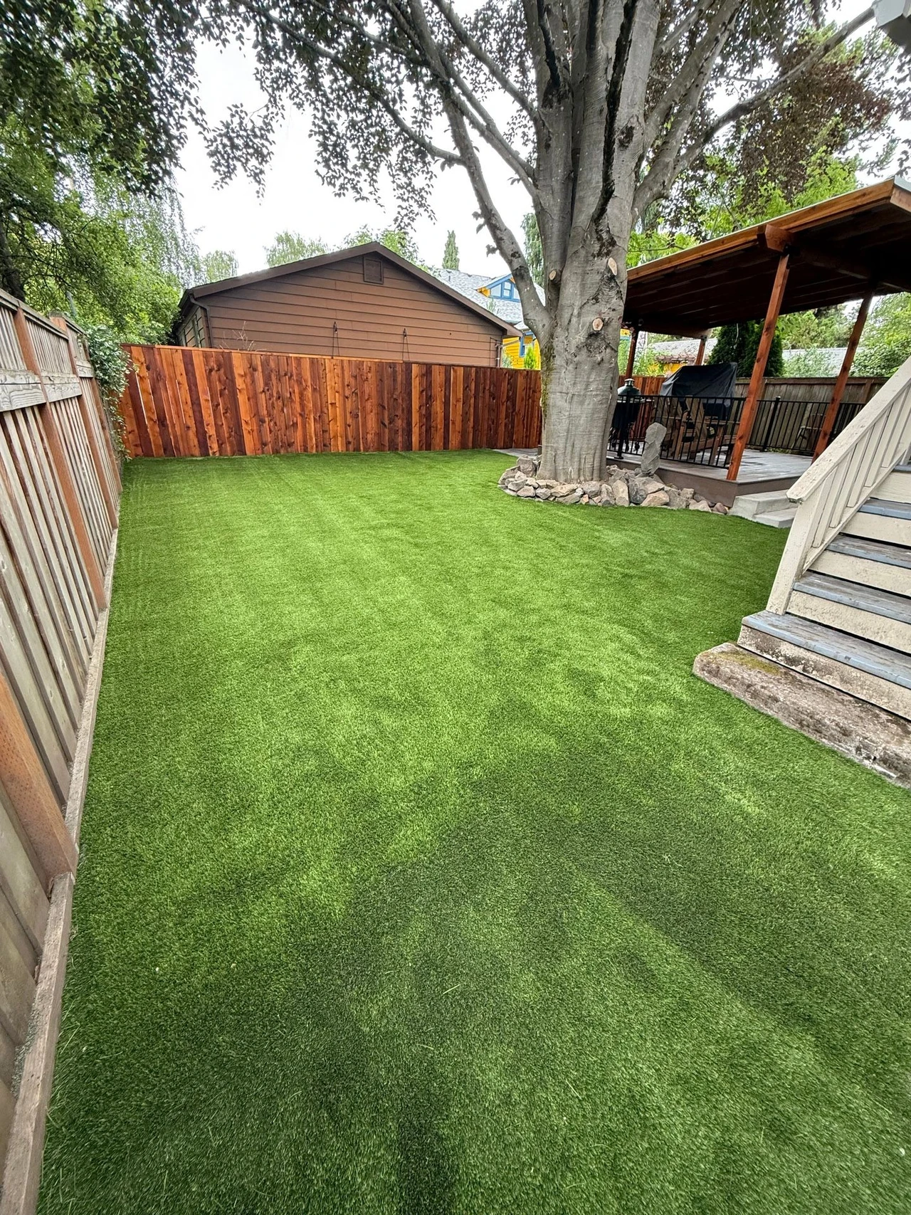 Artificial turf lawn with a fence, tree and gazebo in the background