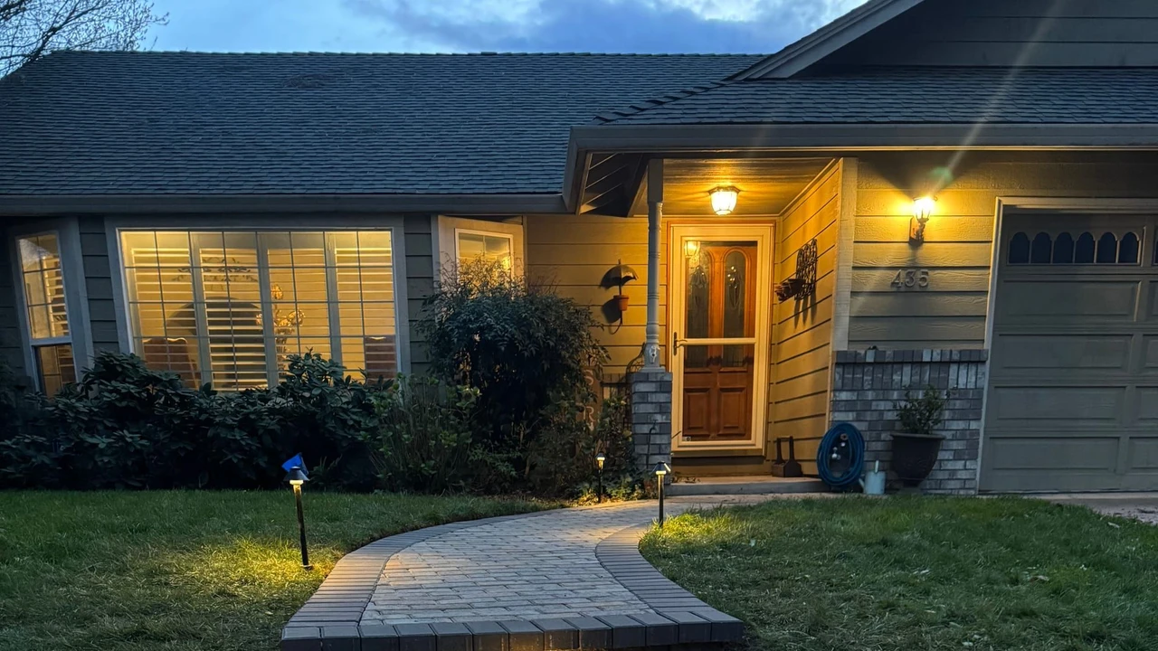 Curved paver front walkway with three raised steps and small встроенные lights leading to a house entrance at dusk, bordered by grass and shrubs, with warm porch and garage lights on.