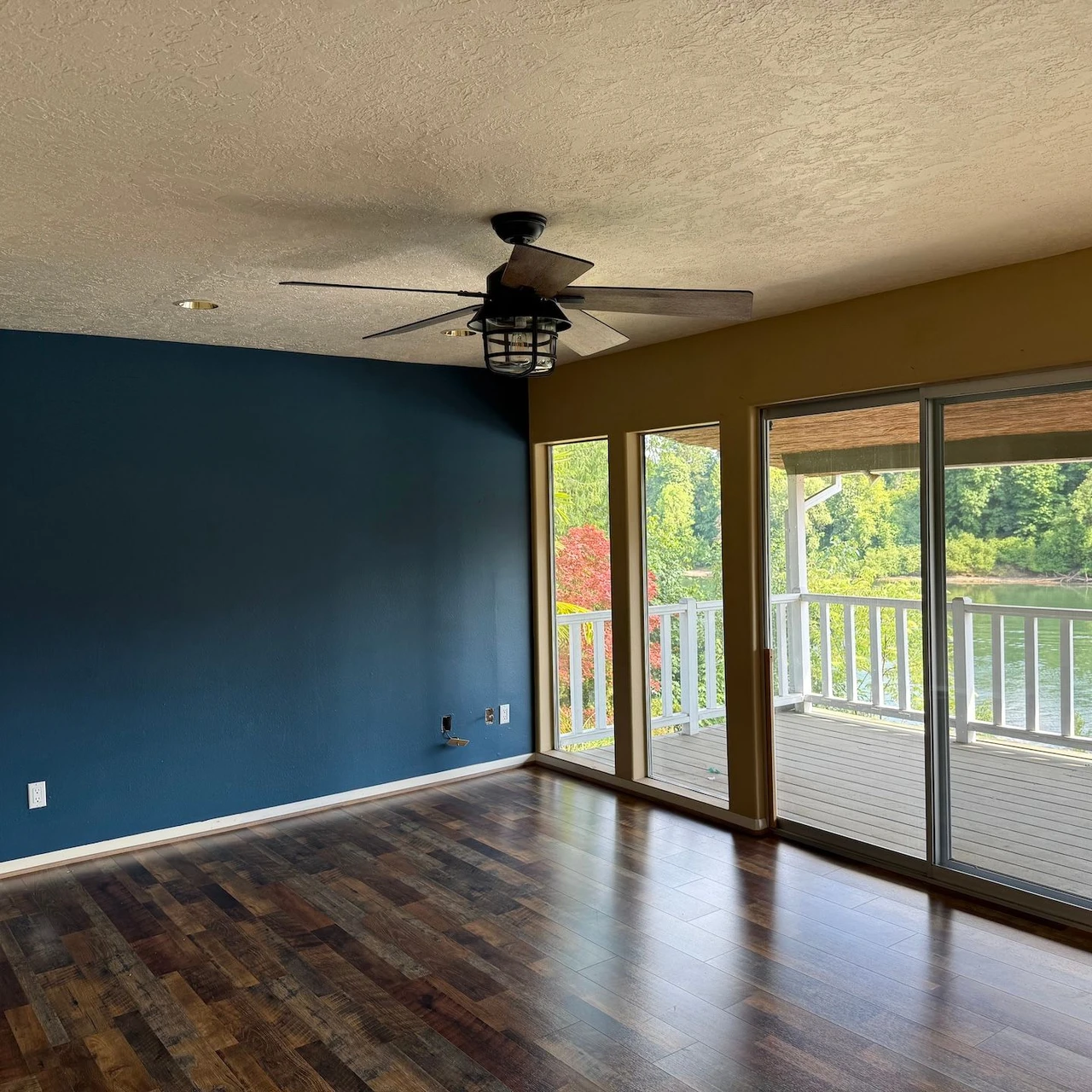 Empty room with a teal wall, dark brown hardwood floors and big windows