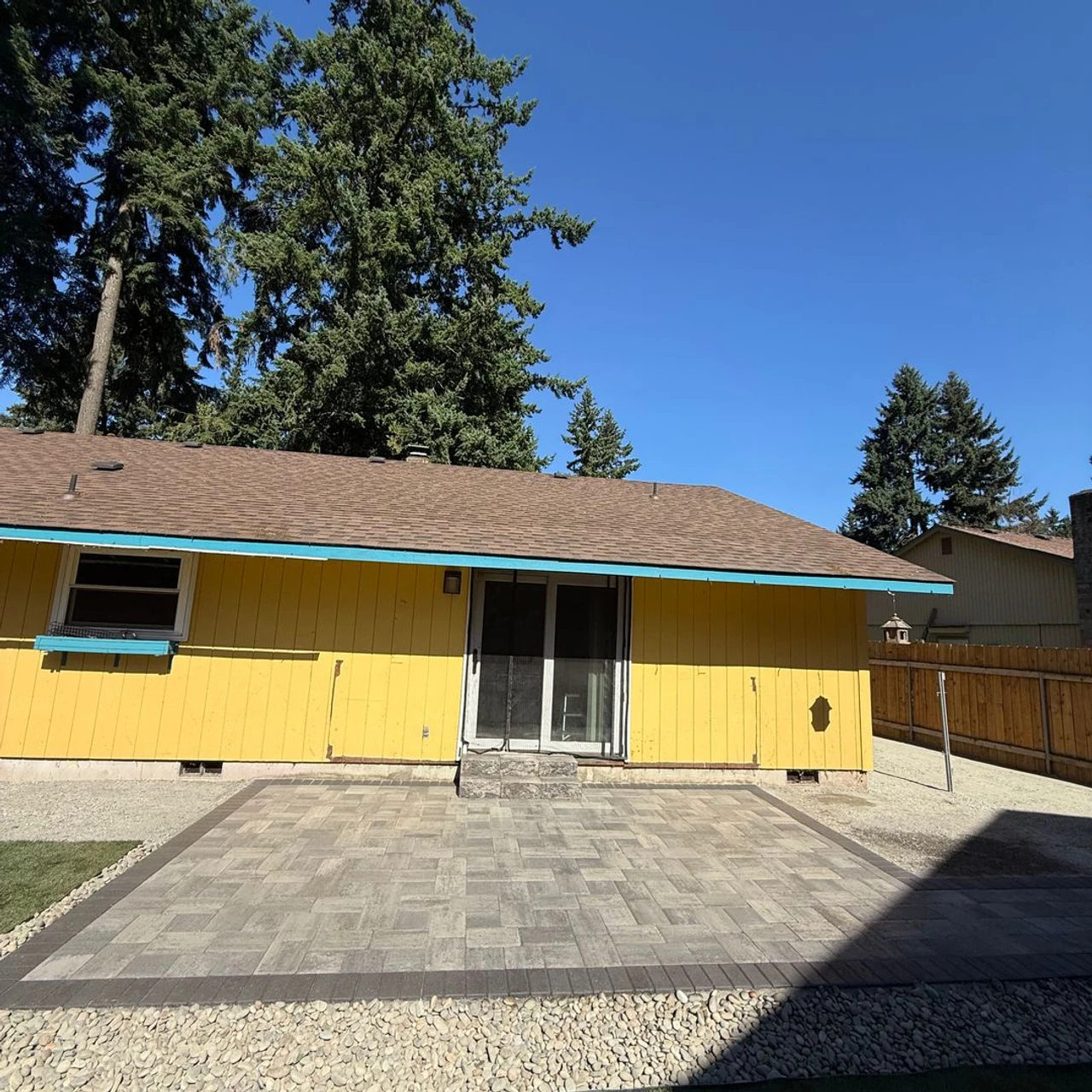 Square paver patio in front of a yellow house