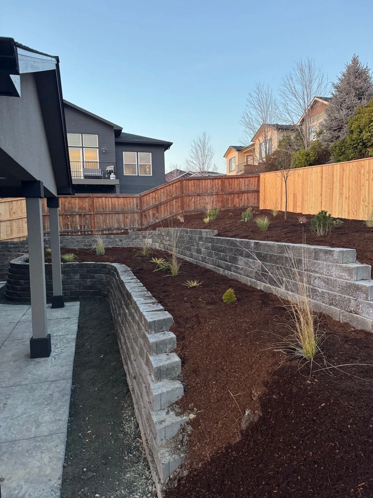 Terraced backyard with two retaining walls holding wood chip gardens. Gardens contain shrubs and other small plants 