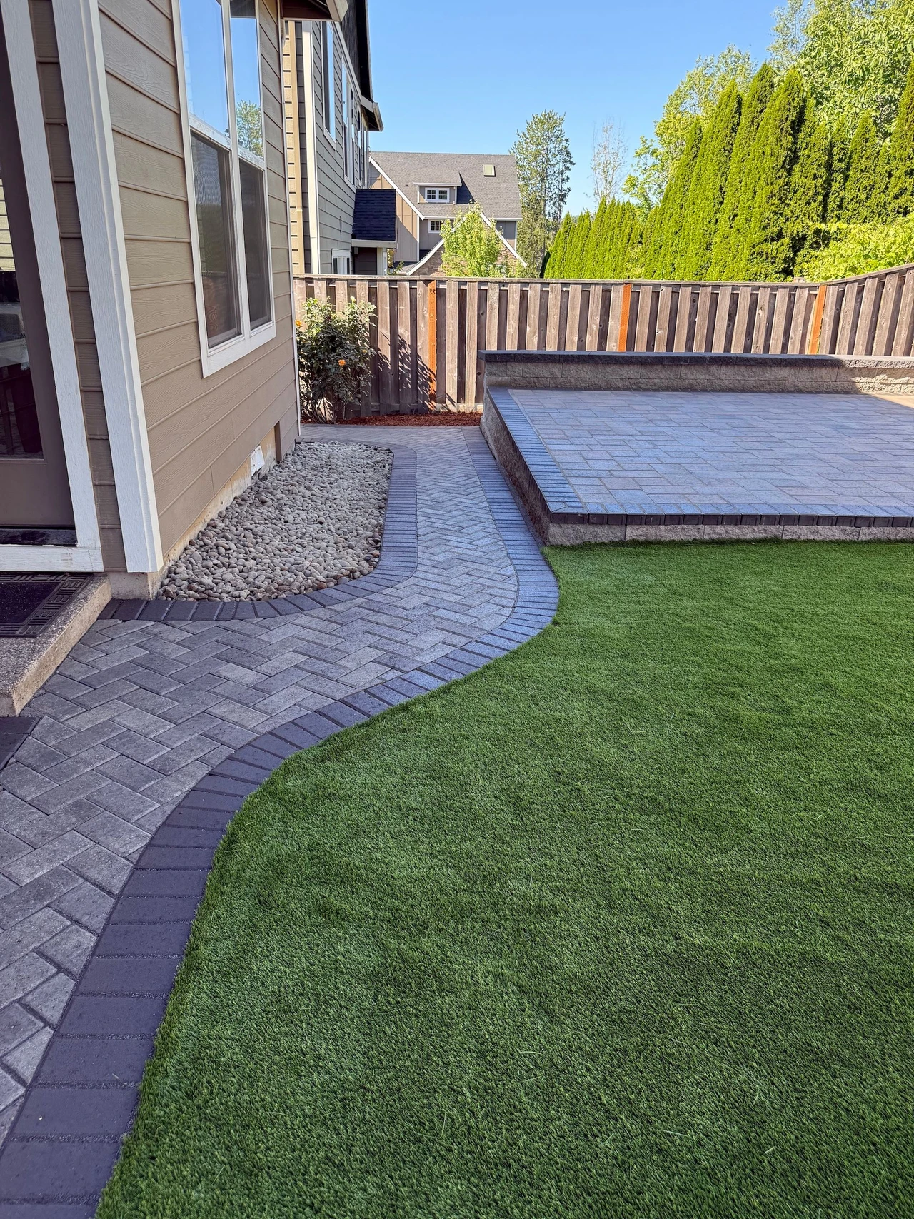 yard with green turf, a raised patio and walkway to the left