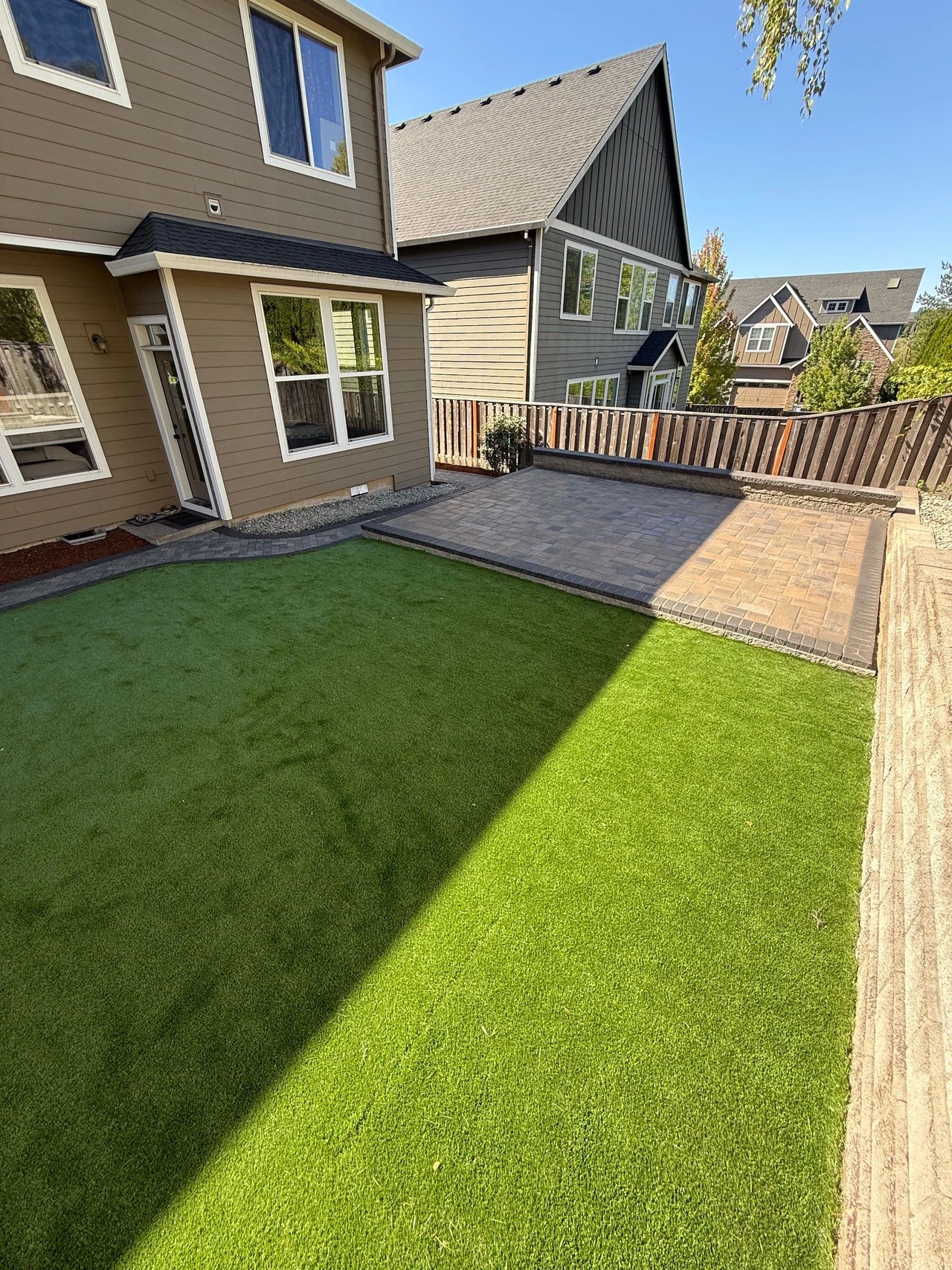 House in the background with artificial turf and a patio in the yard