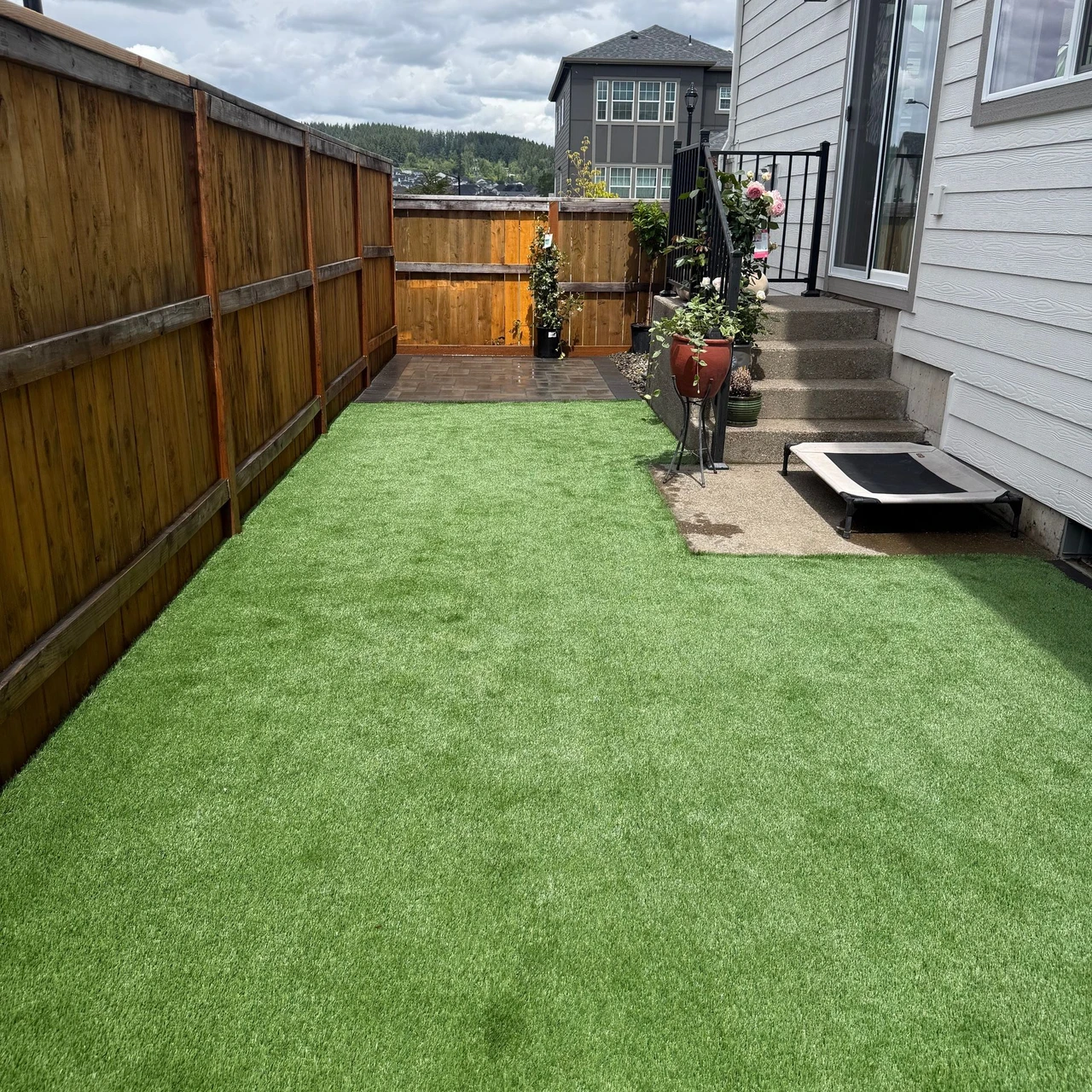 Green Artificial turf with a brown wooden fence and a staircase in the back, leading up to a house