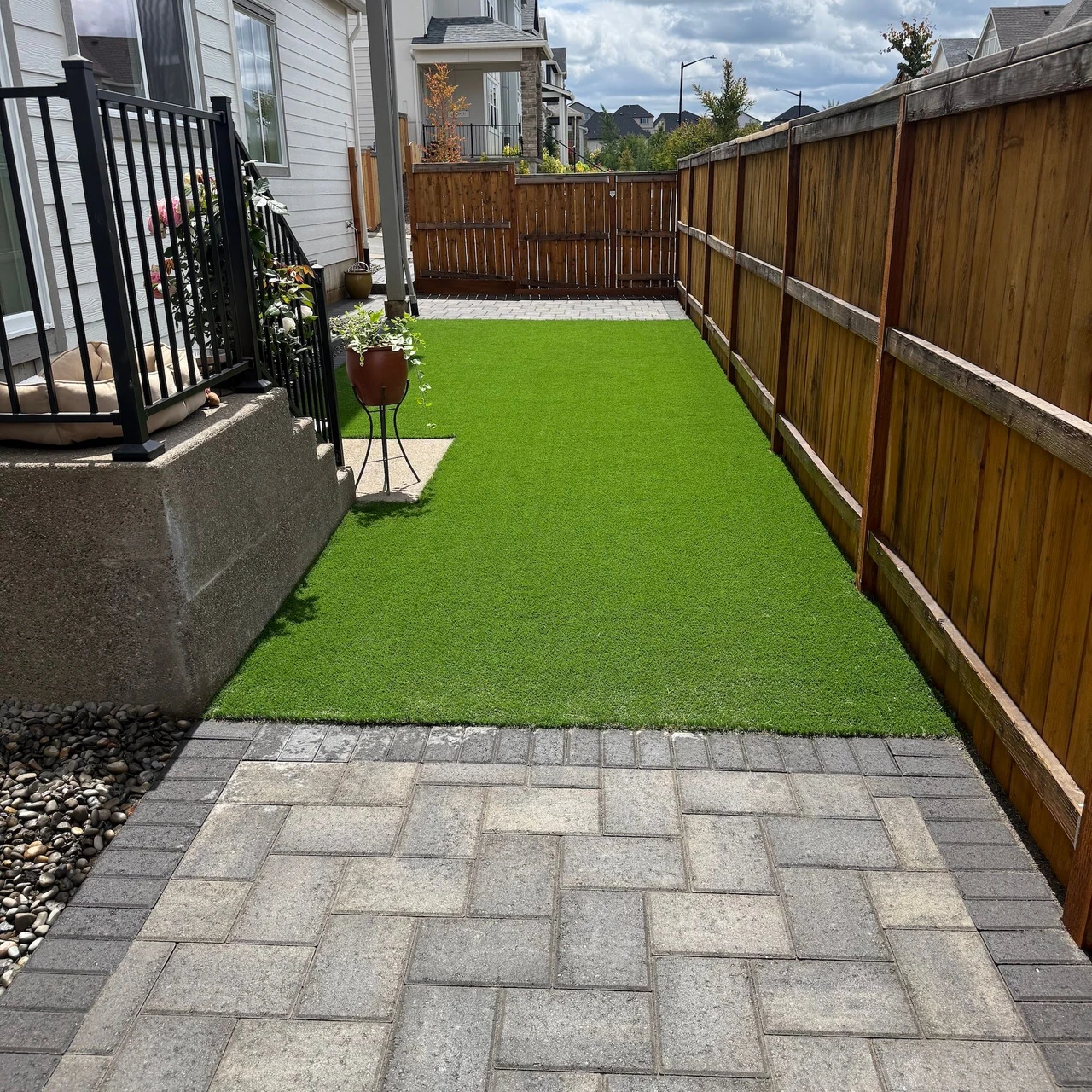Small paver patio with a wooden fence to the right and artificial turf in front