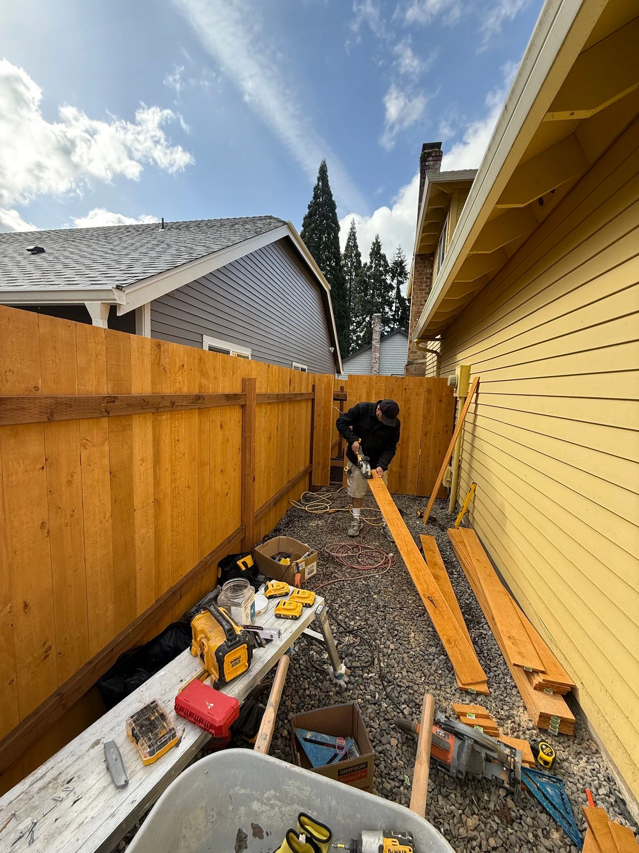 Worker cutting wooden pieces beside a house to install on fence