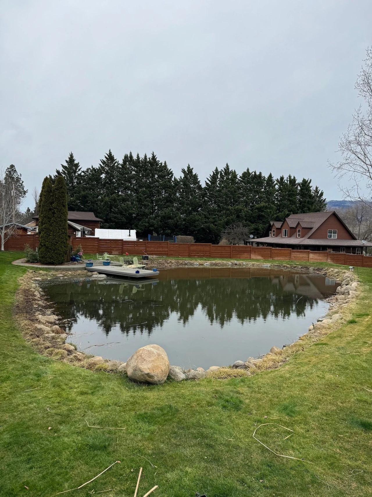 large lawn with pond in the middle and pine trees in background