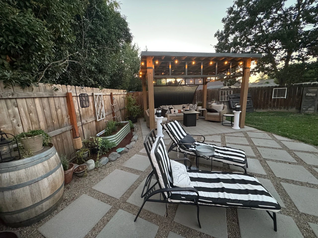 Square paver patio with gravel in-fill. Lawn chairs are placed on top and there is a pergola in the background
