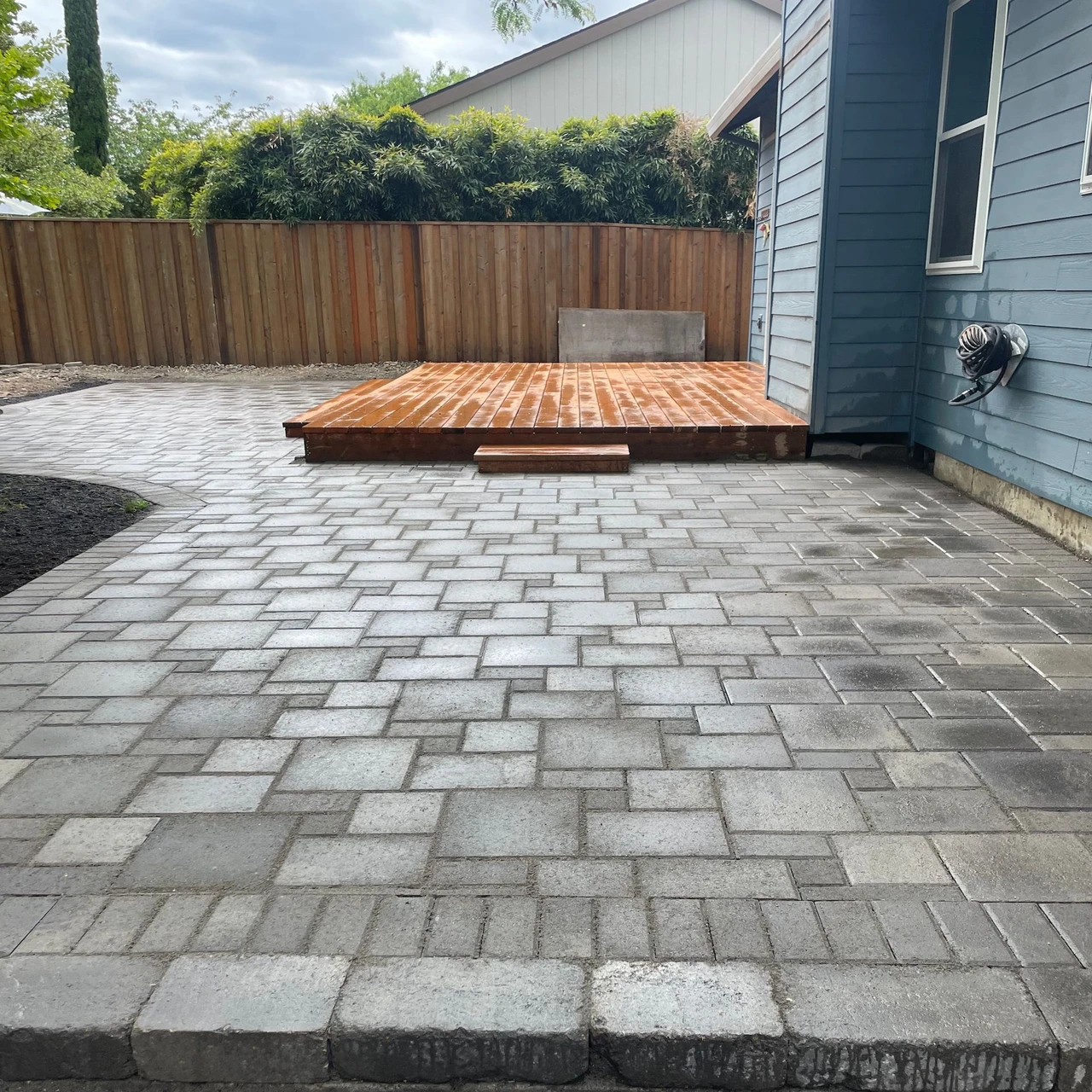 Side view of a paver patio with a small wooden deck