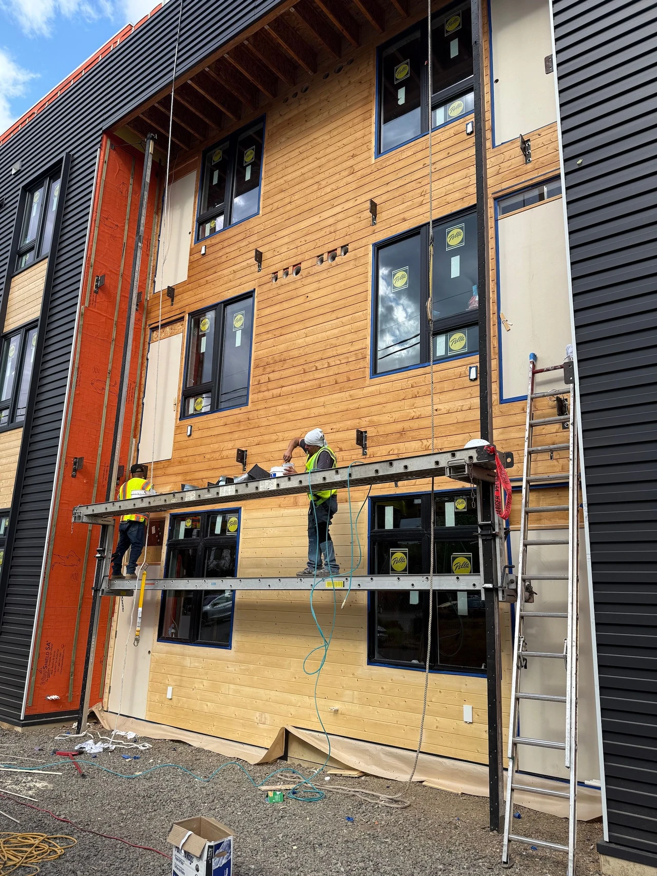 Workers on scaffolding applying stain to wooden siding