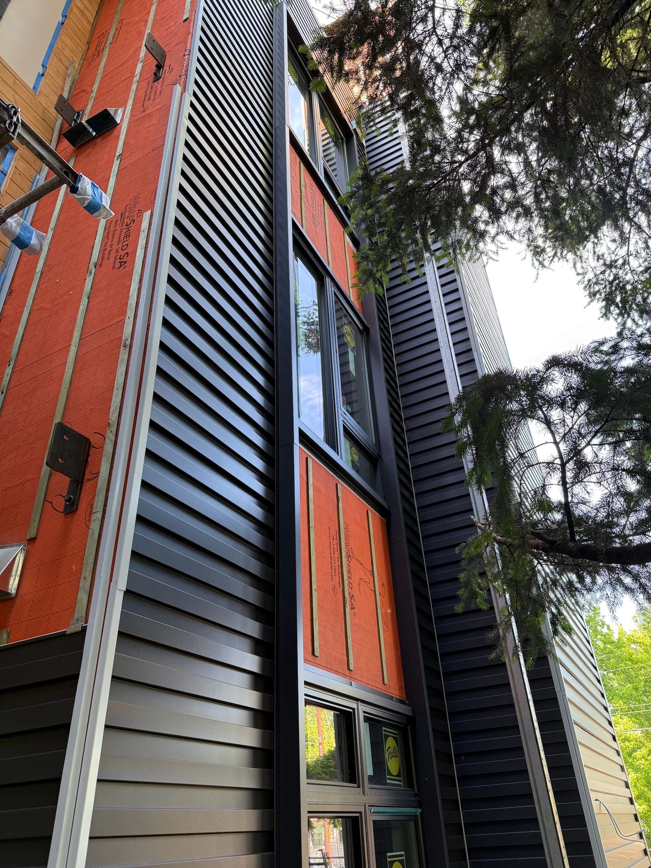 The side of a building with black siding material and orange underlayer showing