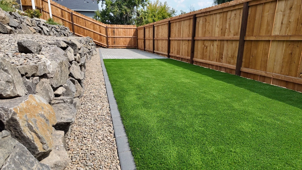 Bright green turf with a tall wooden fence in the background and rock retaining wall to the left